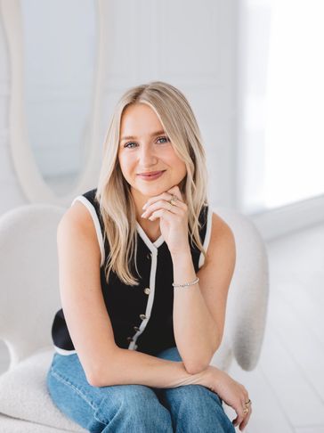 Smiling young woman sitting on a white chair in a bright room.
