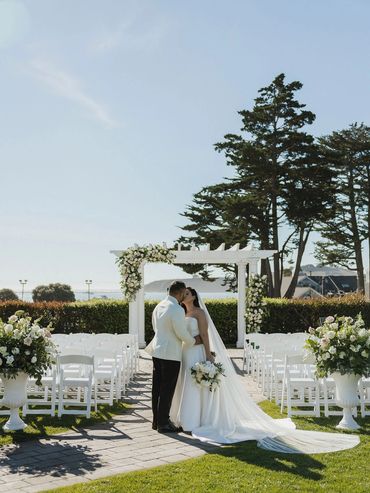 bride groom kiss between floral urns beneath floral arch Oceano Hotel and Spa Half Moon Bay, CA