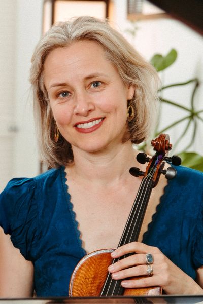 A smiling woman holding a violin indoors.