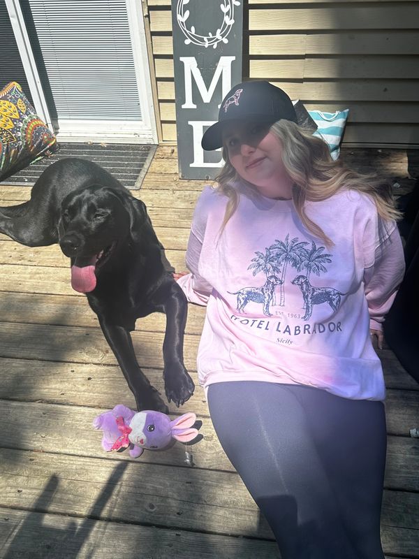 Girl in a pink sweatshirt with a black dog on a wooden deck.