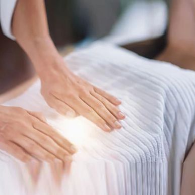 Hands performing Reiki healing on a person lying down.