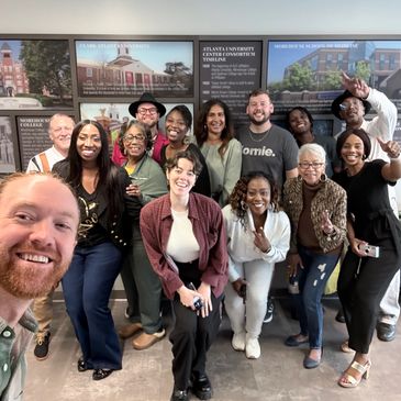 A diverse group smiling and posing for a friendly group selfie indoors.