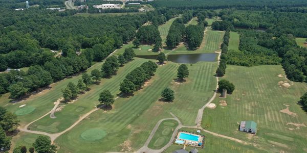 Aerial view of a golf course with a pool and clubhouse surrounded by trees.