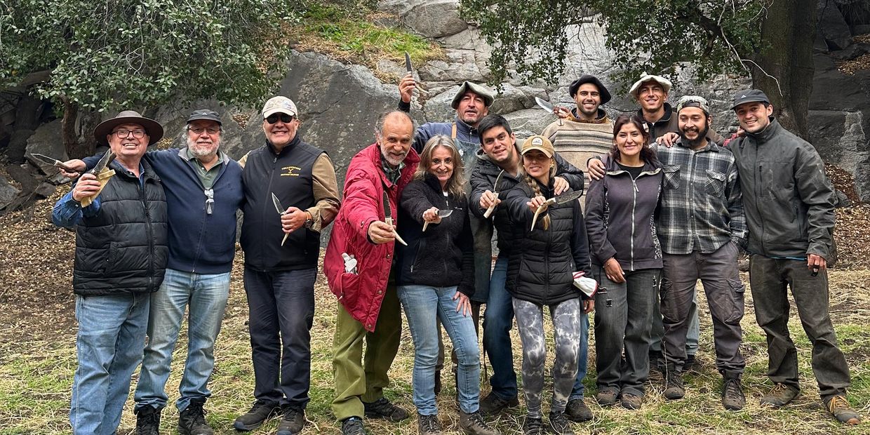 A group of people outdoors holding knives, smiling together in front of rocks.