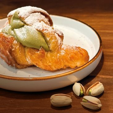 Croissant filled with pistachio cream, dusted with powdered sugar, served on a plate with pistachios beside it.