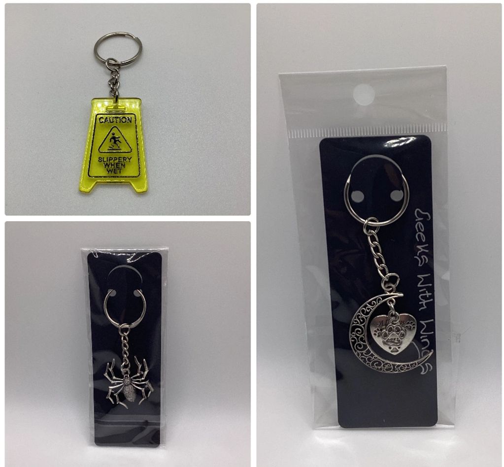 Three different keychains: caution sign, spider, and crescent moon with heart.
