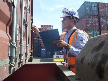 Worker inspecting a shipping container with clipboard and helmet.