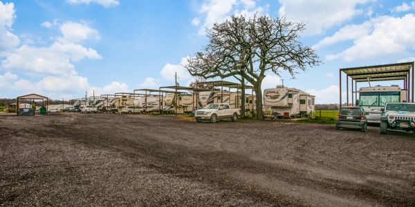 Row of RVs parked with cars under a partly cloudy sky.