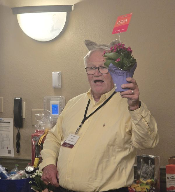 Elderly man holding a potted flower, wearing a yellow shirt and cat ears.