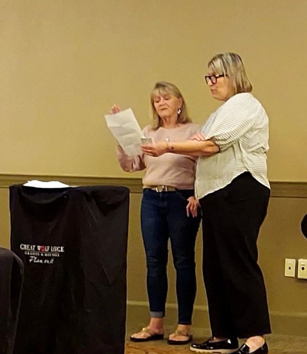 Two women standing and reading from paper in a room.