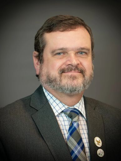 Professional headshot of a man in a suit and plaid tie.