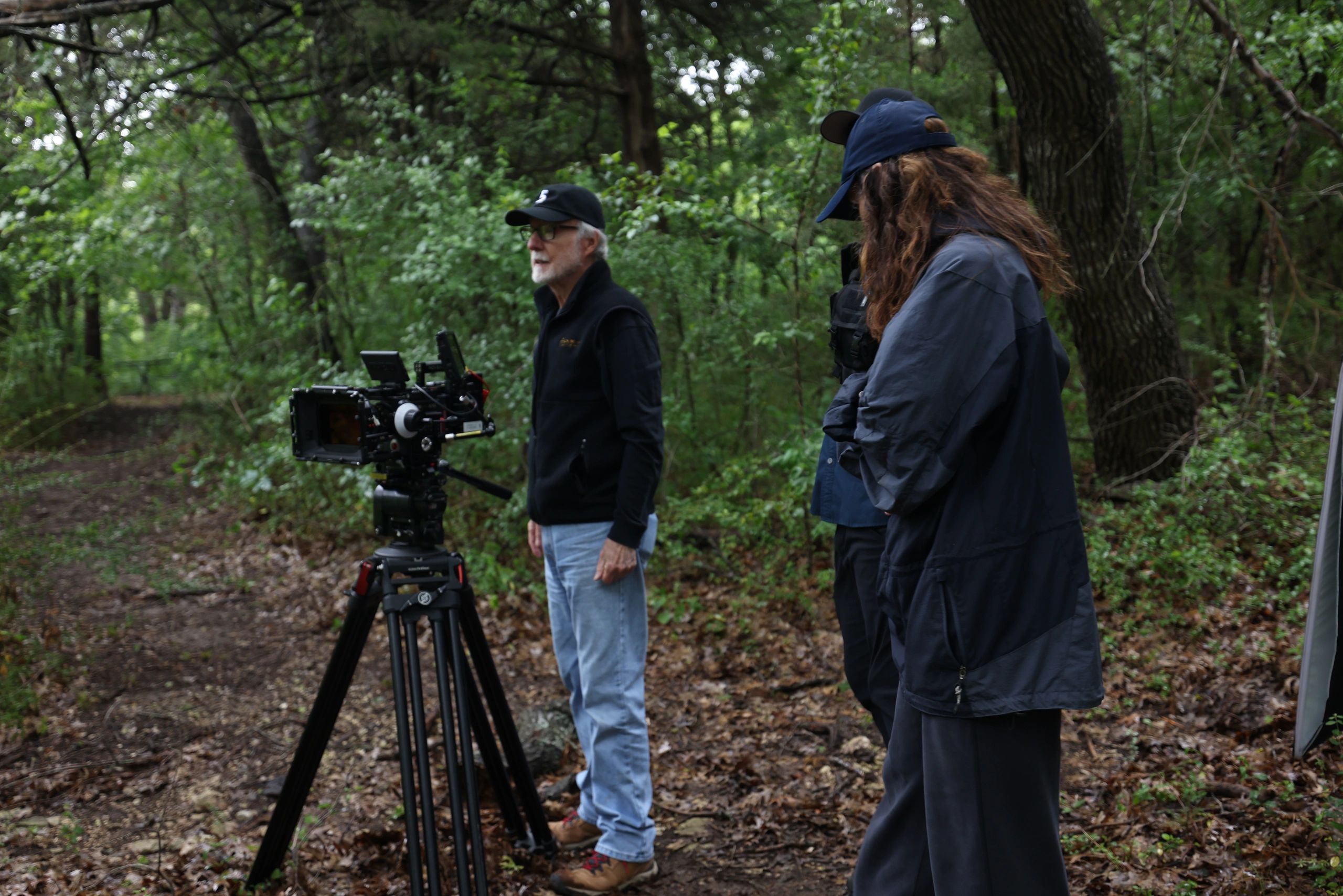Two people with hats filming in a green forest with professional camera equipment.