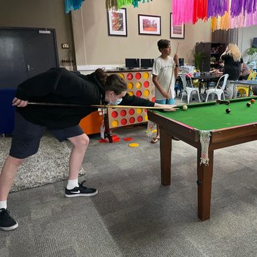People playing pool and giant Connect Four in a colorful indoor setting.