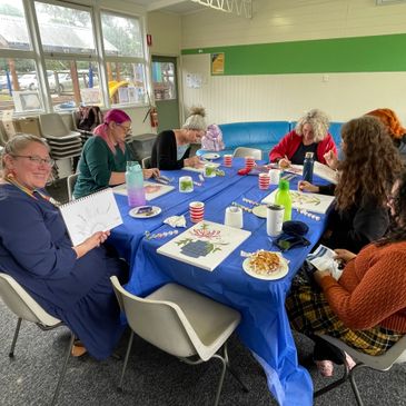 Group of women engaged in a painting and drawing session around a table.