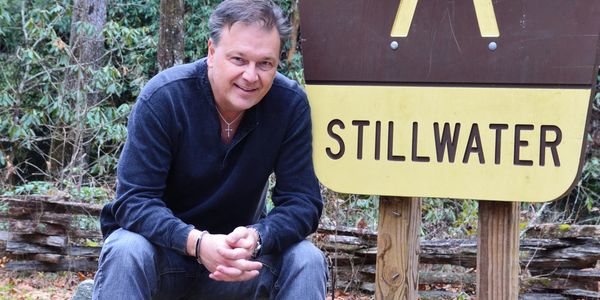 Man crouching near a Stillwater sign outdoors.