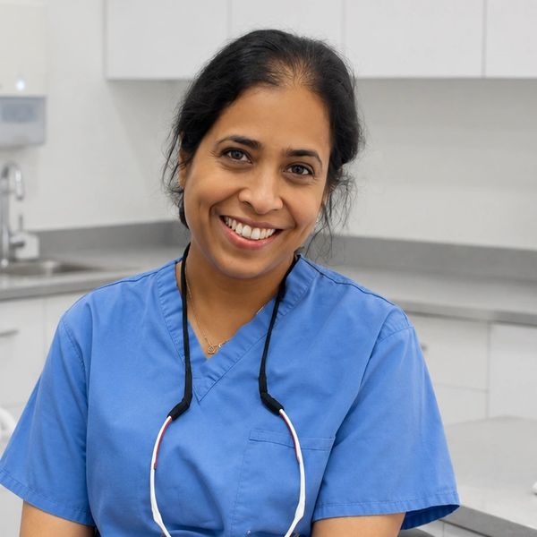 Smiling female healthcare professional in blue scrubs in a clinical setting.
