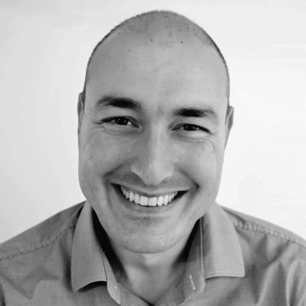 Smiling bald man in a collared shirt against a plain background.
