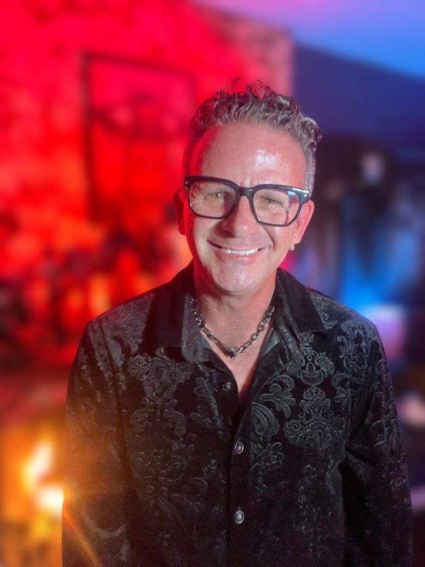 Man with glasses smiling in a warmly lit, colorful background.