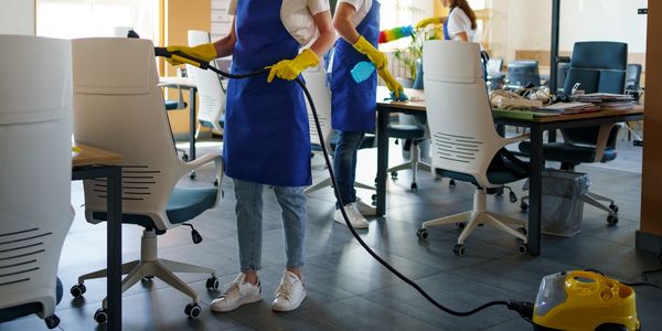Three cleaners in blue aprons cleaning an office space with white chairs.