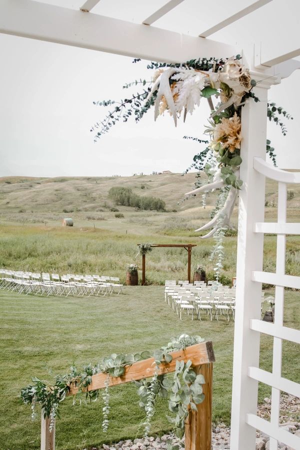 Outdoor wedding setup with white chairs and floral decorations on a pergola.