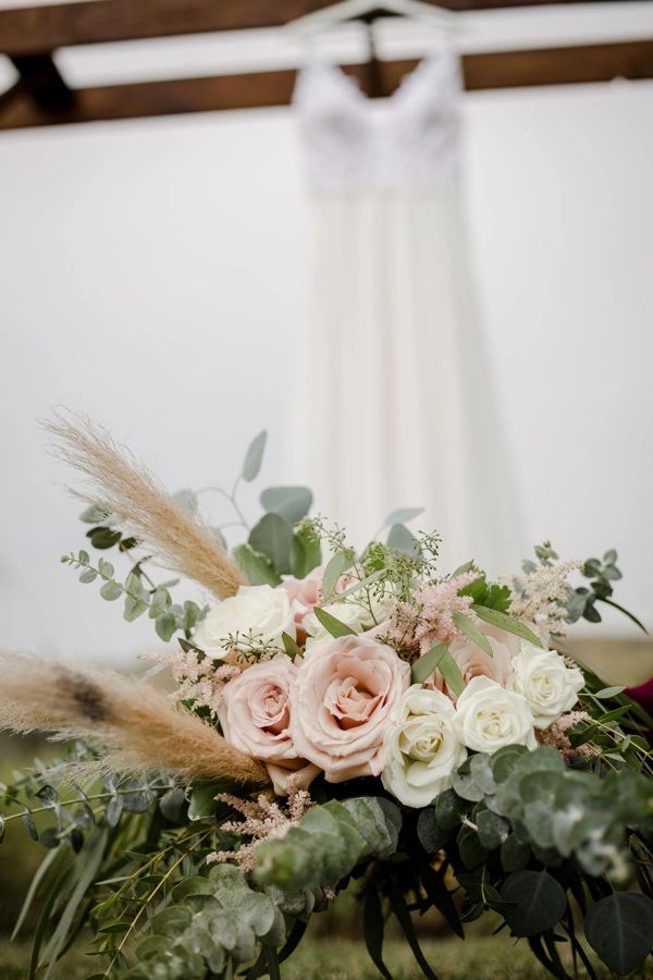 Elegant bouquet with soft pink and white roses in front of a blurred wedding dress.
