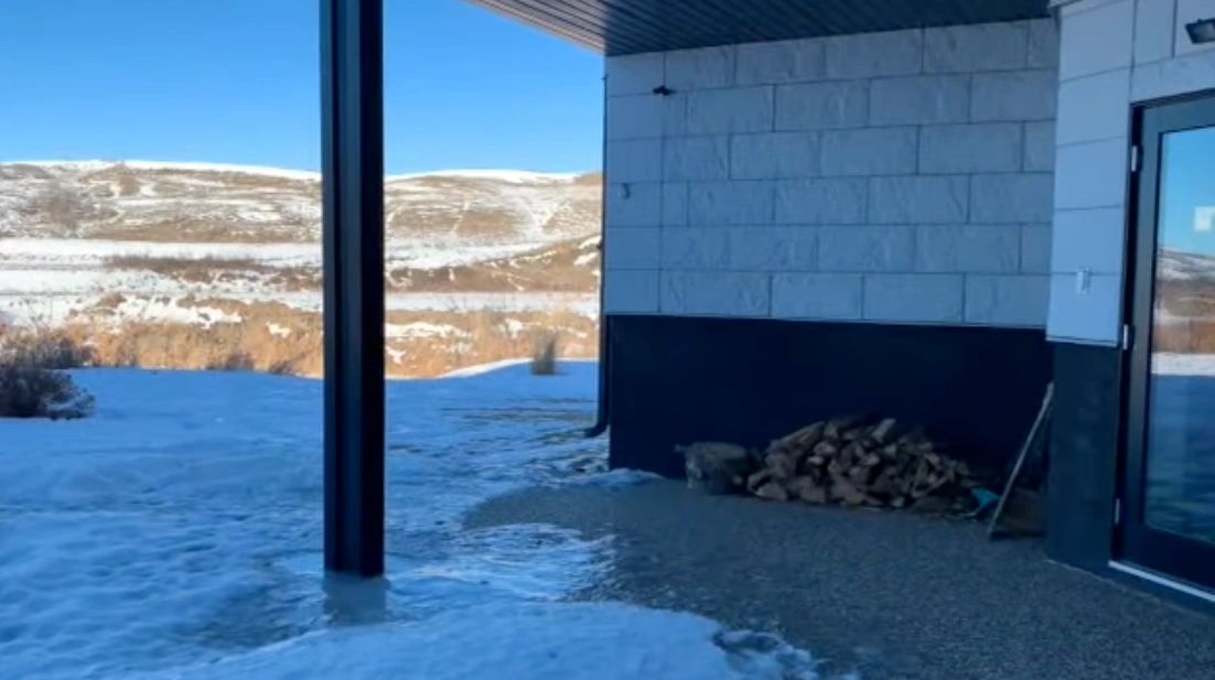 Snow melts near a house, creating puddles.