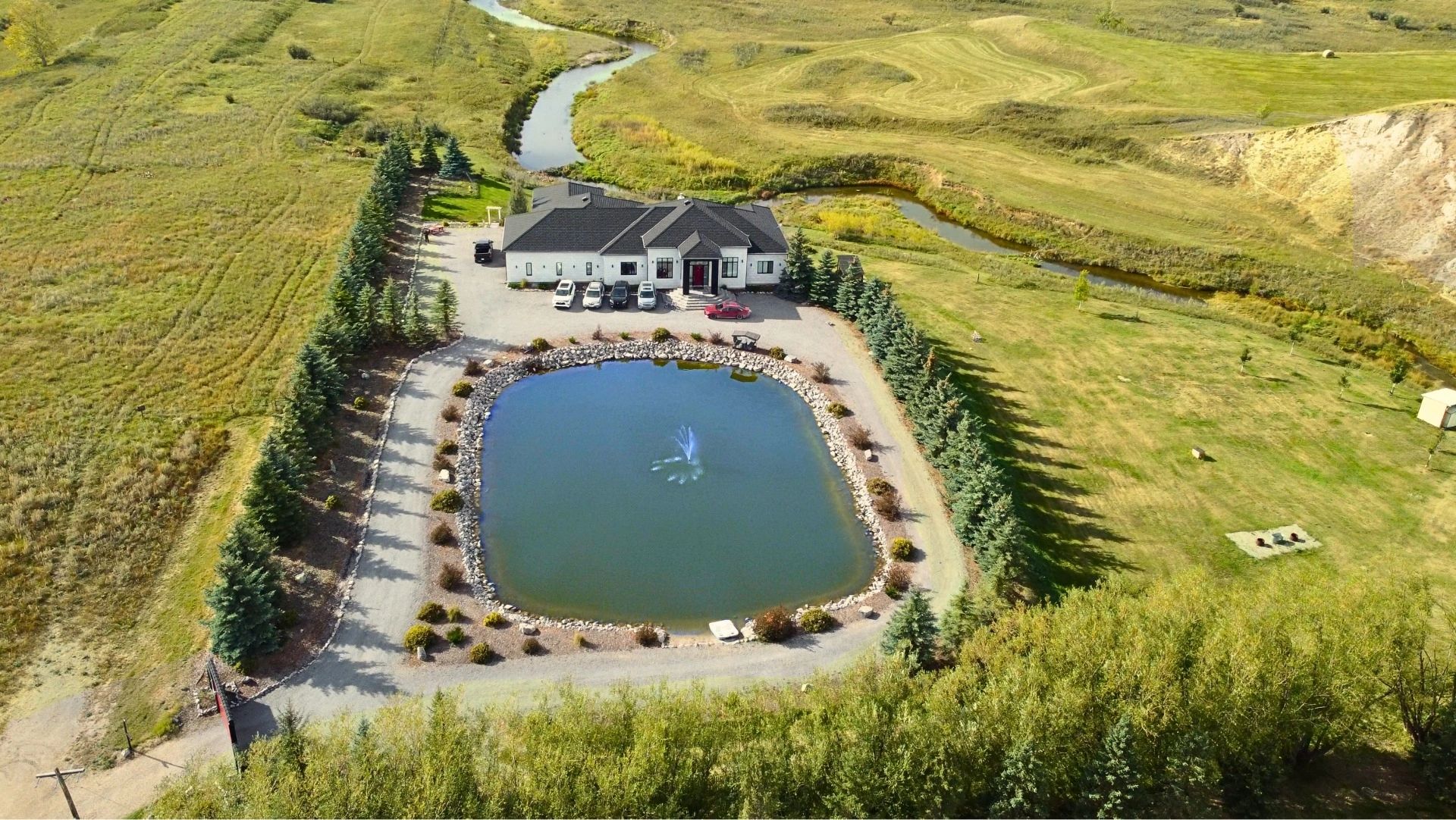 A house with a pond and fountain surrounded by trees and fields.