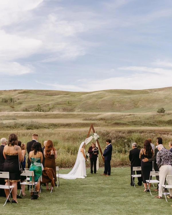 Outdoor wedding ceremony with bride and groom under a floral arch.