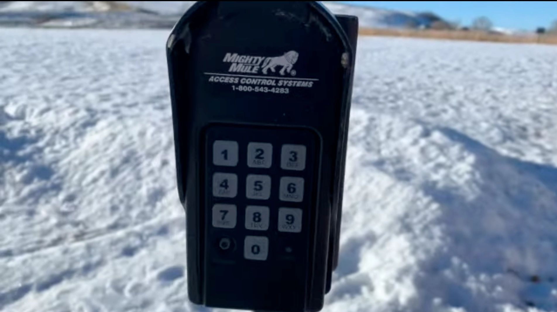 Black keypad access control system in a snowy landscape.