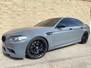 A BMW M5 with a 3M-Certified Tint wrap parked in front of a modern building.