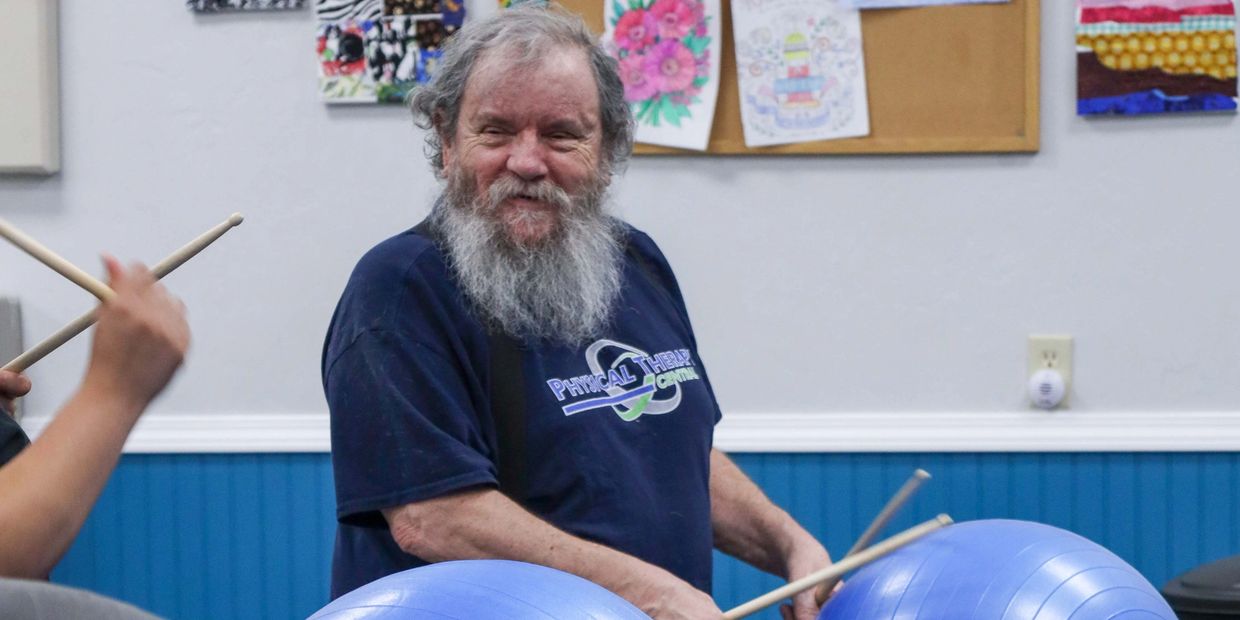 Elderly man enjoying drumming on exercise balls in a cheerful setting.