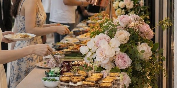 People serving themselves desserts and food at a buffet with floral decorations.