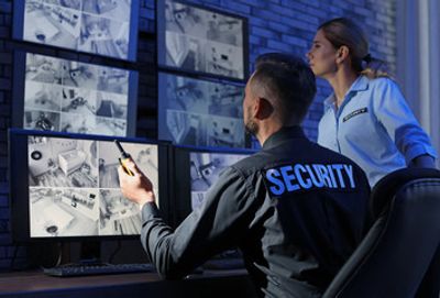 Security personnel monitoring surveillance cameras in a control room.
