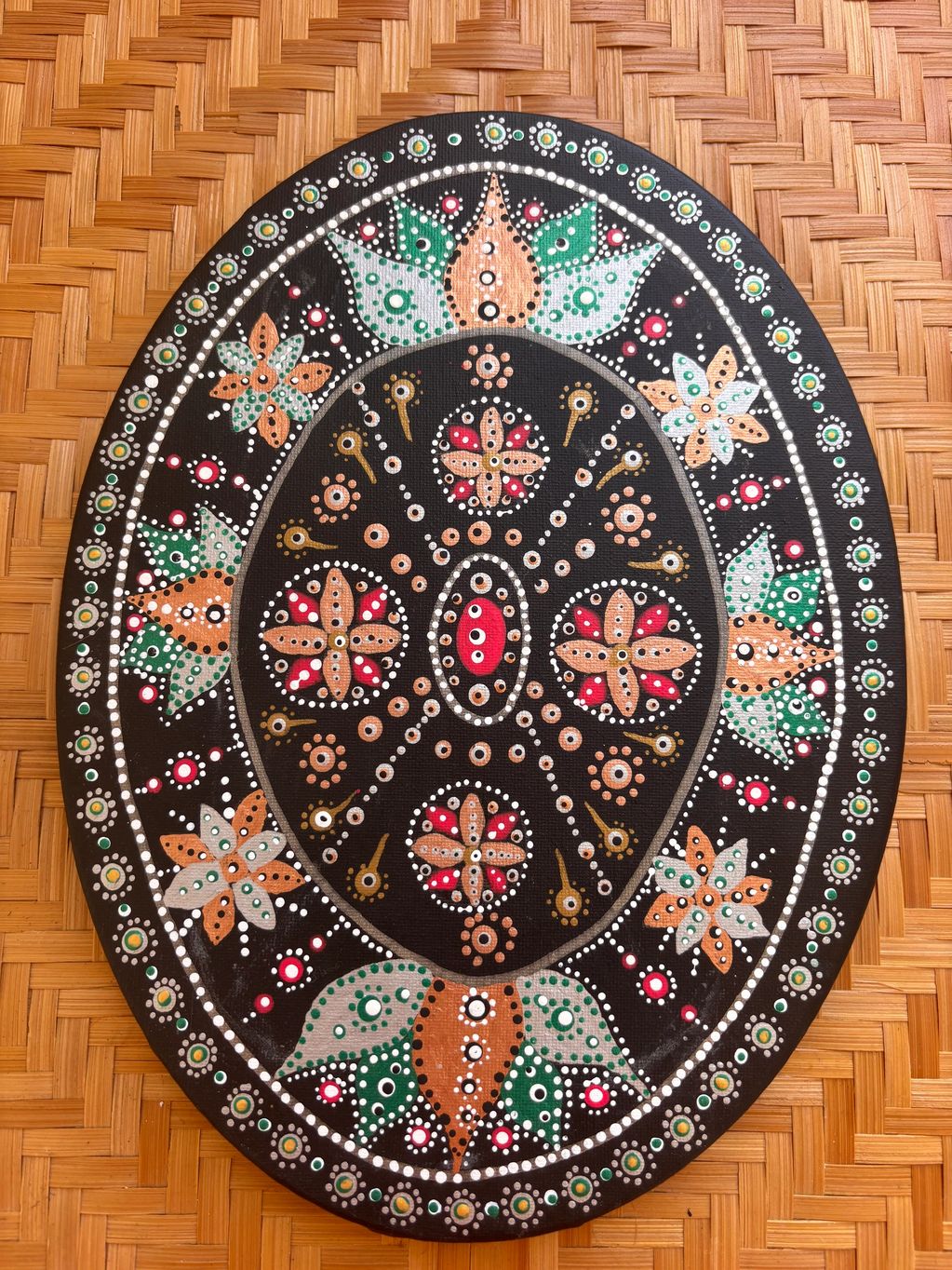 Oval-shaped mandala art with floral patterns on a woven mat.