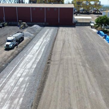 Terreno amplio con camión y material apilado junto a un edificio.