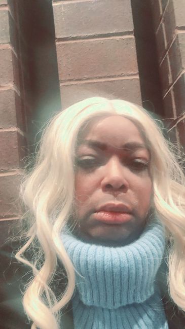 Woman with long blonde hair and blue sweater against brick background.