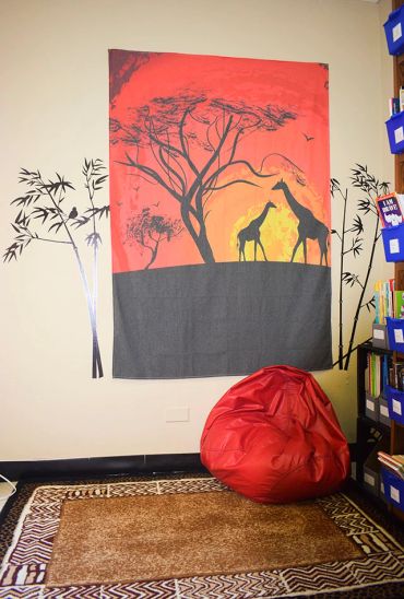 A cozy reading nook with a giraffe wall hanging and red bean bag.