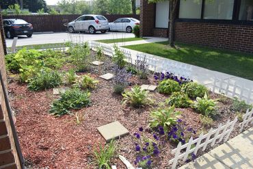 A small garden with plants and flowers bordered by a white fence.