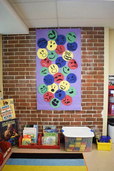 Classroom wall display with colorful emoticons above book crates.