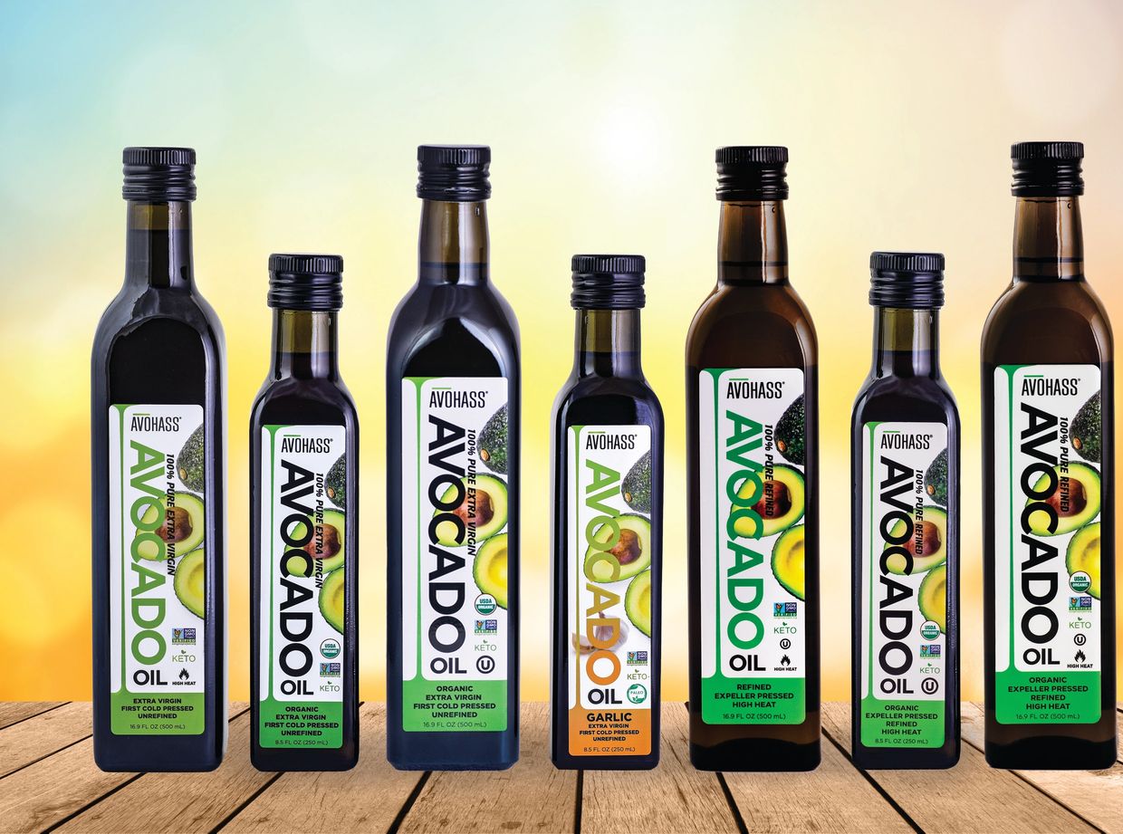 Variety of Avohass avocado oil bottles on wooden surface with bright background.