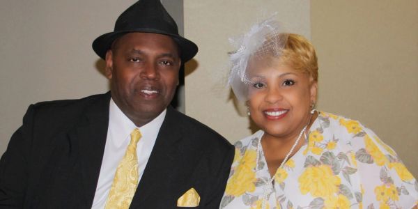 A couple dressed elegantly in black and yellow attire, smiling for the camera.