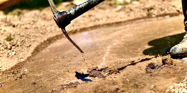 A person using a pickaxe to break ground near a water source.