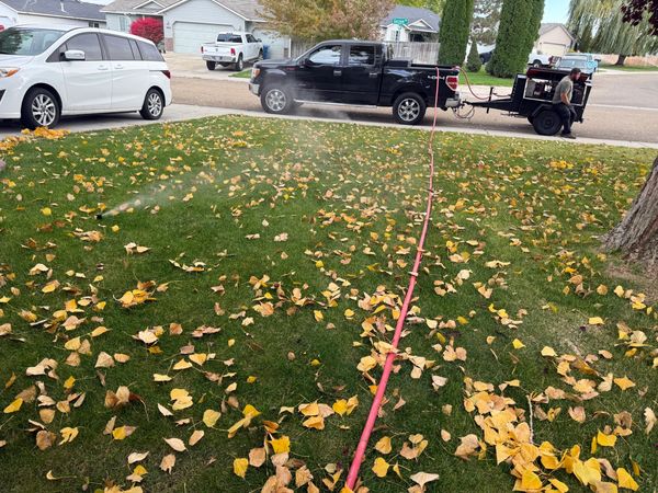 A lawn being watered with a sprinkler connected to a truck and trailer setup.