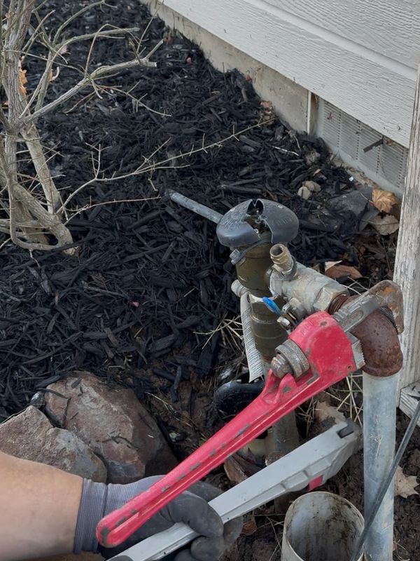 Person using a red pipe wrench to fix outdoor plumbing near a house.
