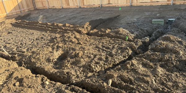 Freshly dug trenches in a backyard with a wooden fence.