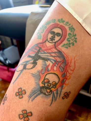 Religious-themed tattoo with skull and flames on arm.