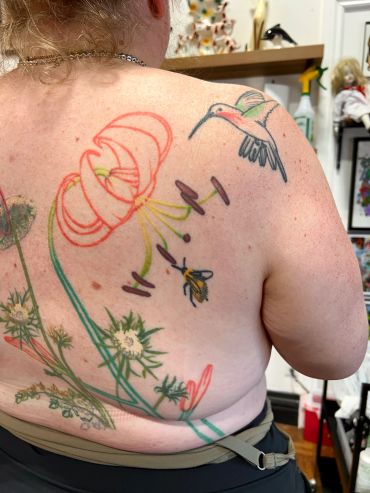 Back tattoo with flowers, hummingbird, and bee.