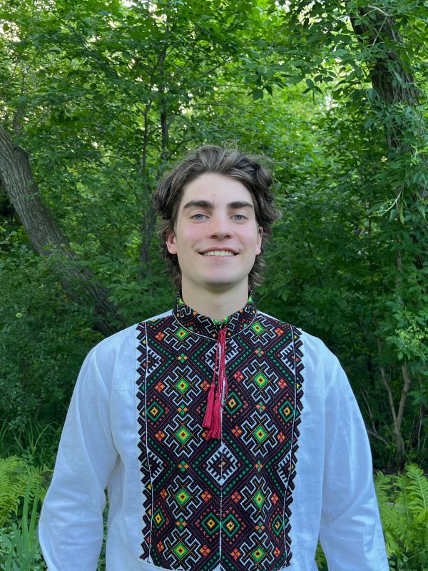Young man wearing a traditional embroidered shirt in a green forest.