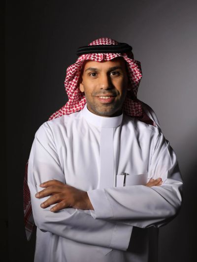 Man in traditional white thobe and red-checkered keffiyeh.