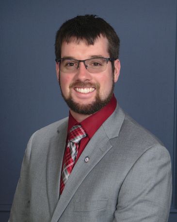 Man smiling in a gray suit and red shirt.